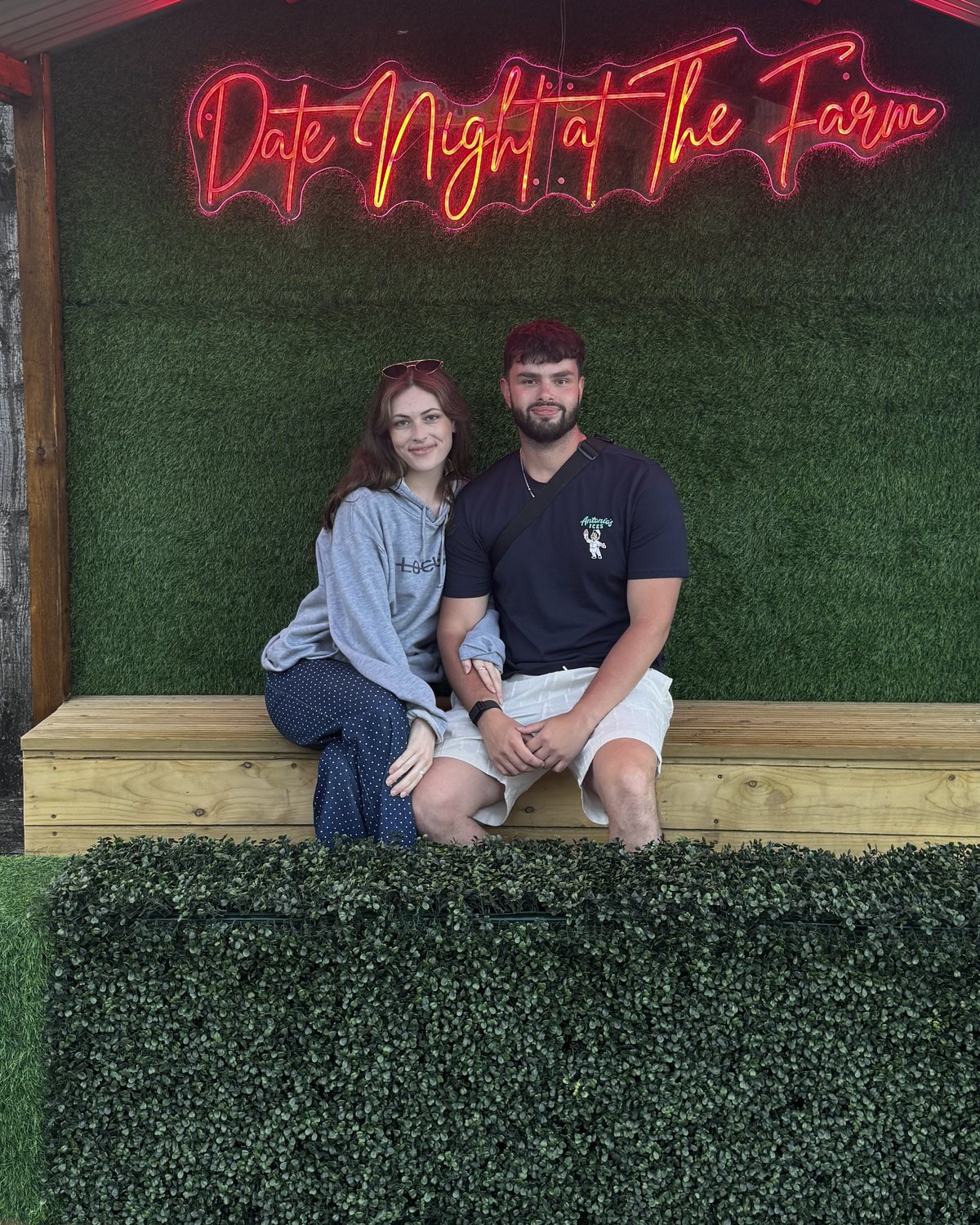 Muírenn and Yil sitting together on a bench under a pink neon sign